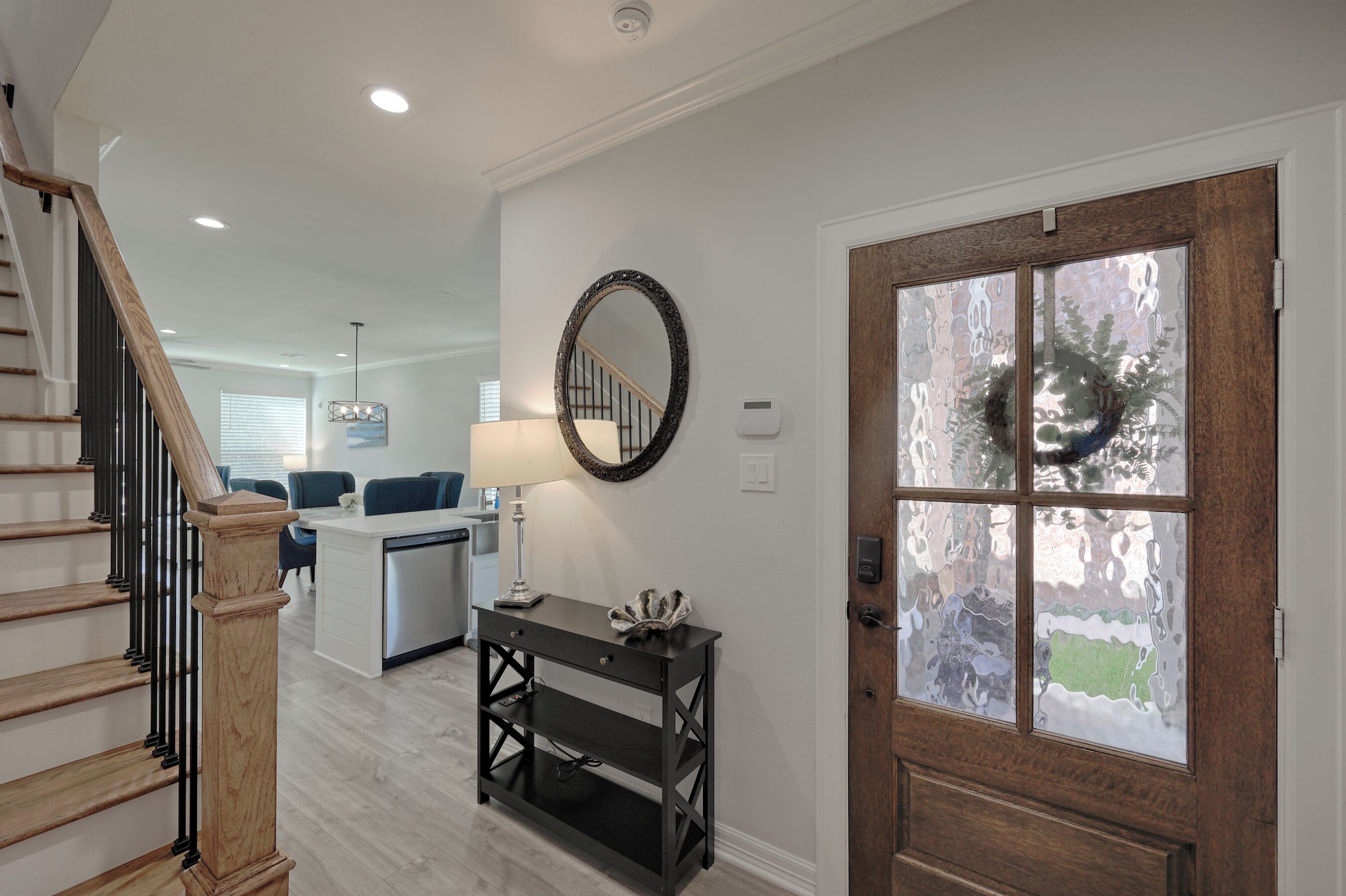 Un interior moderno con una escalera, una zona de cocina y una puerta de madera con paneles de vidrio esmerilado.