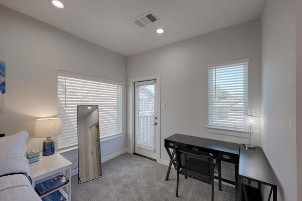 A compact room with a desk, a chair, a lamp, a refrigerator, and a door leading to another room. - Cozy Newer Home Close to Lake Conroe, Pool, Golf Course, Tennis & Country Club! (Montgomery)