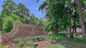 A sign for 'A Club Community' with a landscaped area featuring trees and shrubs. - Cozy 2/2.5 Close to Lake Conroe, Pool, Golf Course, Tennis & Country Club! (Montgomery)