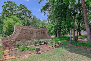 A sign for 'A Club Community' with a landscaped area featuring trees and shrubs. - Cozy 2/2.5 Close to Lake Conroe, Pool, Golf Course, Tennis & Country Club! (Montgomery)