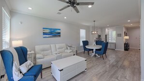 A modern living room with a white sofa, a blue armchair, a dining table with chairs, and a ceiling fan. - Cozy 2/2.5 Close to Lake Conroe, Pool, Golf Course, Tennis & Country Club! (Montgomery)