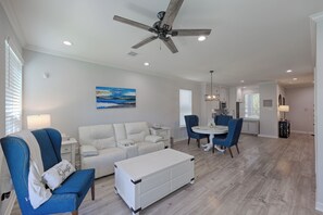 A modern living room with a white sofa, a blue armchair, a dining table with chairs, and a ceiling fan. - Cozy 2/2.5 Close to Lake Conroe, Pool, Golf Course, Tennis & Country Club! (Montgomery)