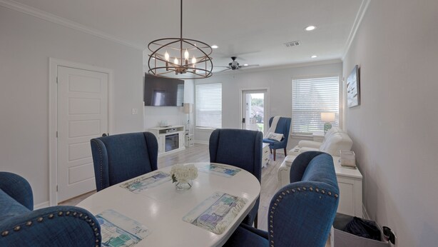 A dining area with a round table, blue upholstered chairs, a chandelier, and a view of the kitchen and living room through the windows. - Cozy 2/2.5 Close to Lake Conroe, Pool, Golf Course, Tennis & Country Club! (Montgomery)