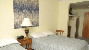 A bedroom with two beds, a nightstand with a lamp, a wooden chair, and a wardrobe.