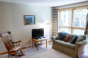 A living room with a television, a rocking chair, a sofa, and a window with curtains.