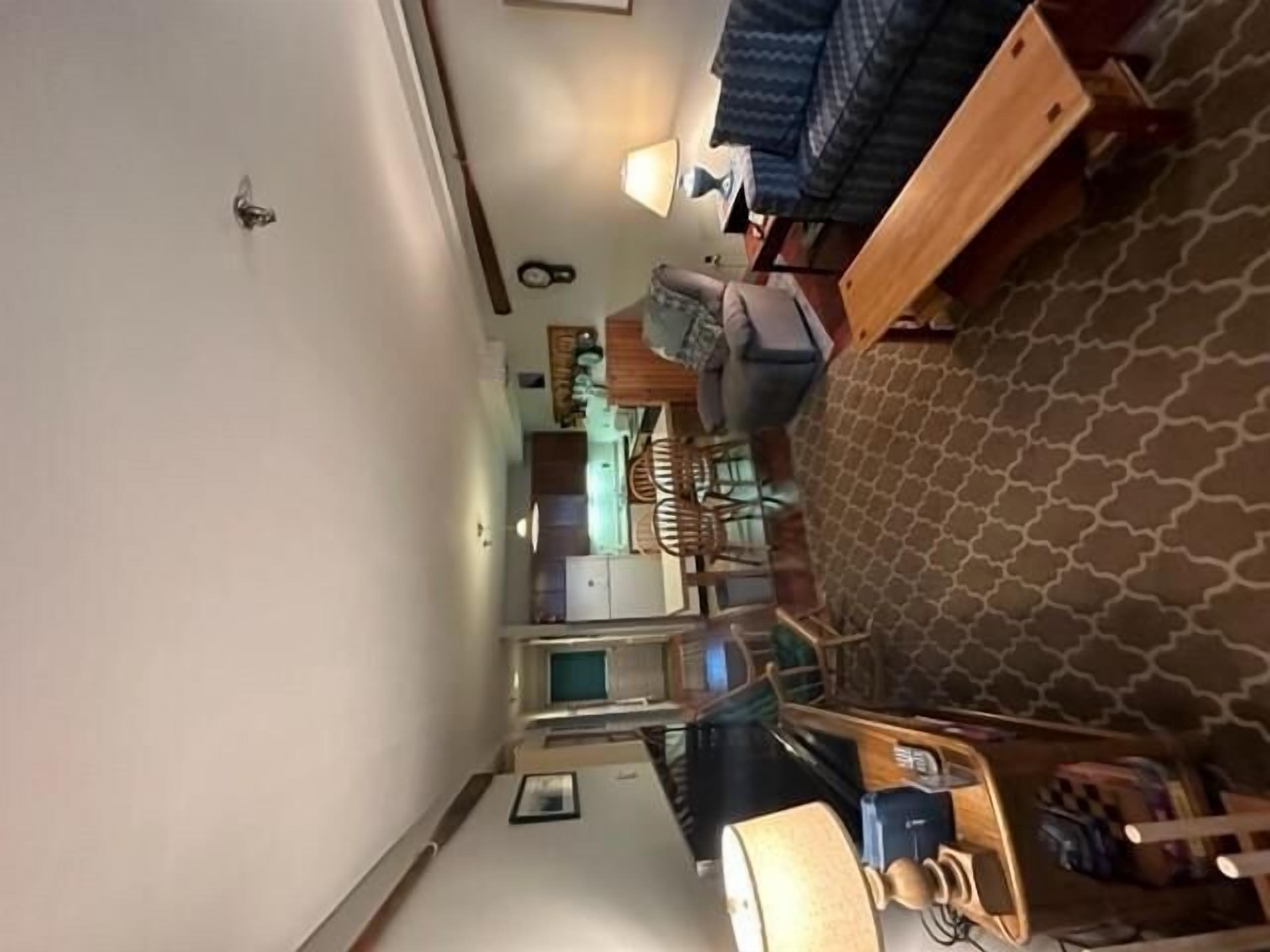 A compact room with a kitchenette, a bed with a patterned headboard, and a small seating area.