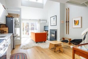 Een moderne keuken met een fornuis, koelkast en houten keukenkastjes. Er is een zithoek met een tafel en stoelen, en een open haard.