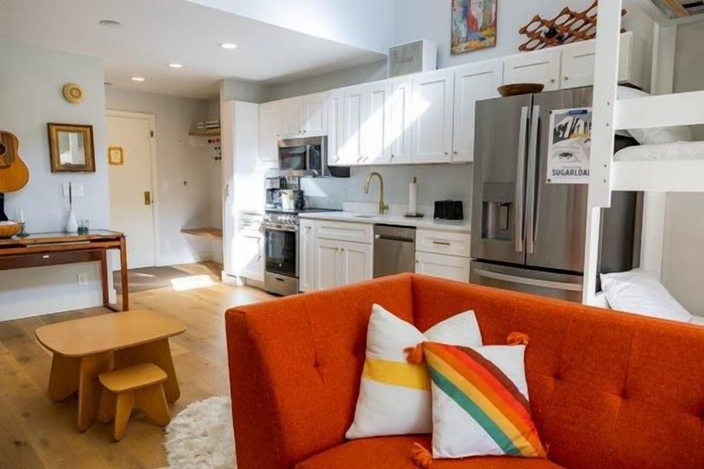 Un espacio habitable compacto con kitchenette, comedor y un sofá con un cojín de arcoíris.