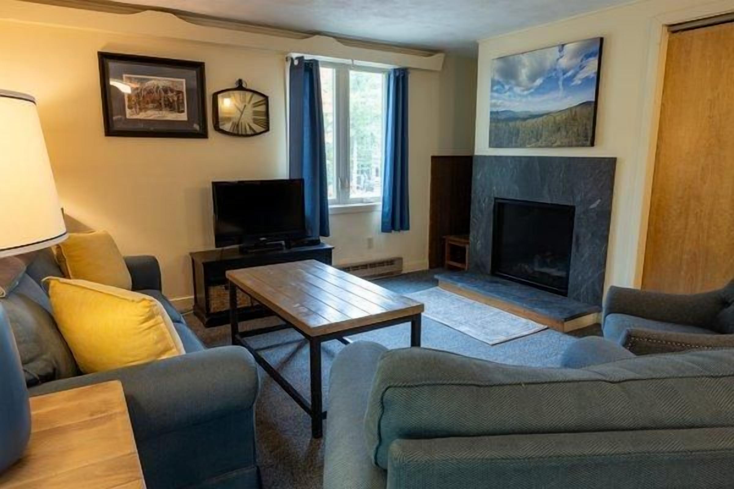 Een woonkamer met een bank, salontafel, televisie, open haard en een raam met gordijnen.