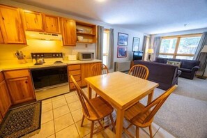 A compact kitchen with wooden cabinets, a dining table, and chairs. - Sugarloaf Mountain Snowbrook Village C2524 (Carrabassett Vly)