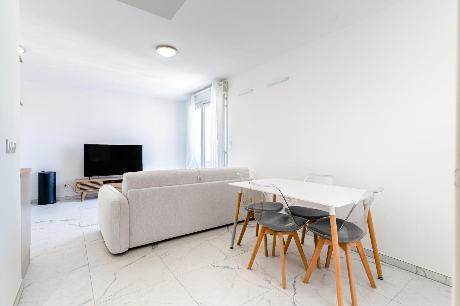 Un salon moderne avec un canapé, un téléviseur et une table à manger avec des chaises.