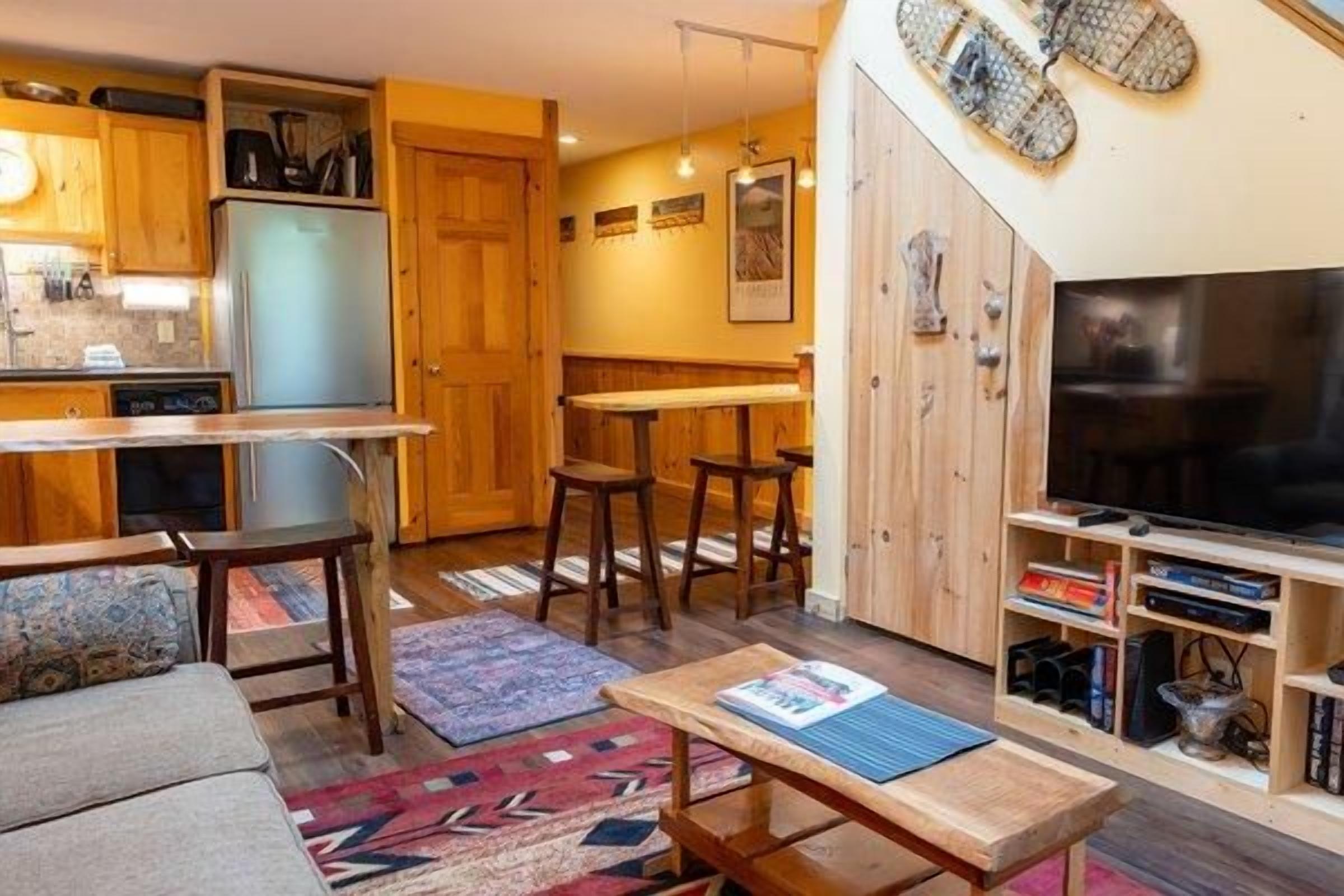 Un espacio habitable compacto con kitchenette, comedor, zona de estar con sofá y televisión.