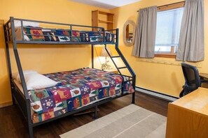 Ein Etagenbett mit einer farbenfrohen Steppdecke, ein Schreibtisch, ein Stuhl, eine Lampe und ein Fenster mit Vorhängen.