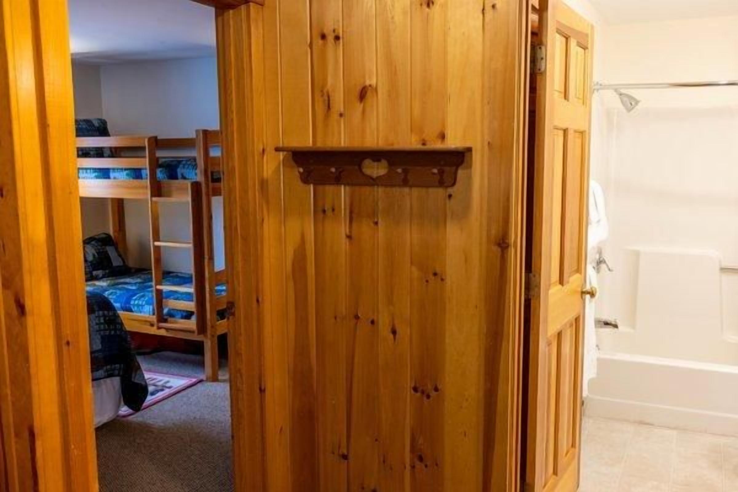 Puerta de madera que da a una habitación con literas y una bañera.