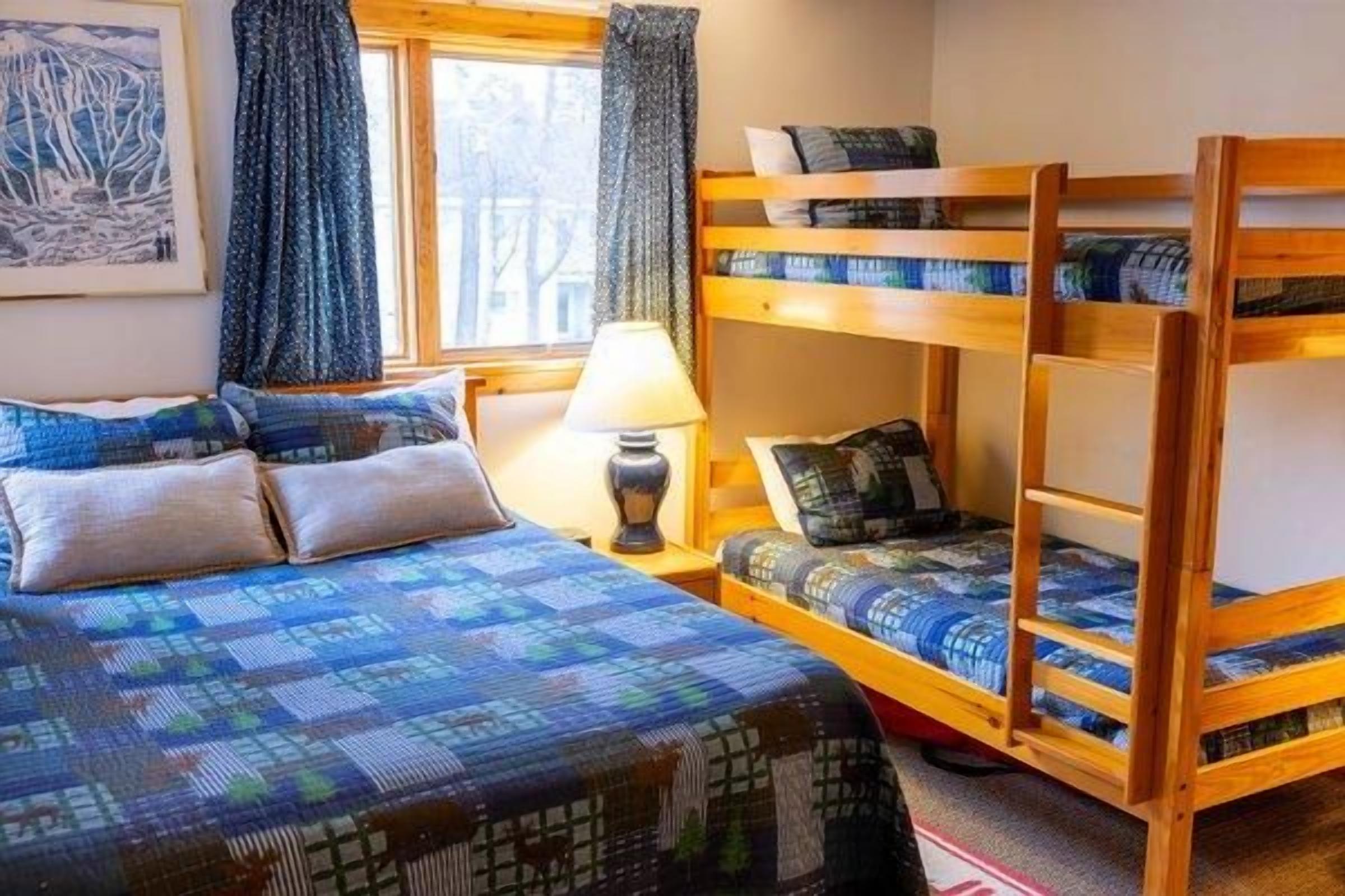 Ein Zimmer mit Etagenbett, Einzelbett, Lampe und einem Vorhangfenster.