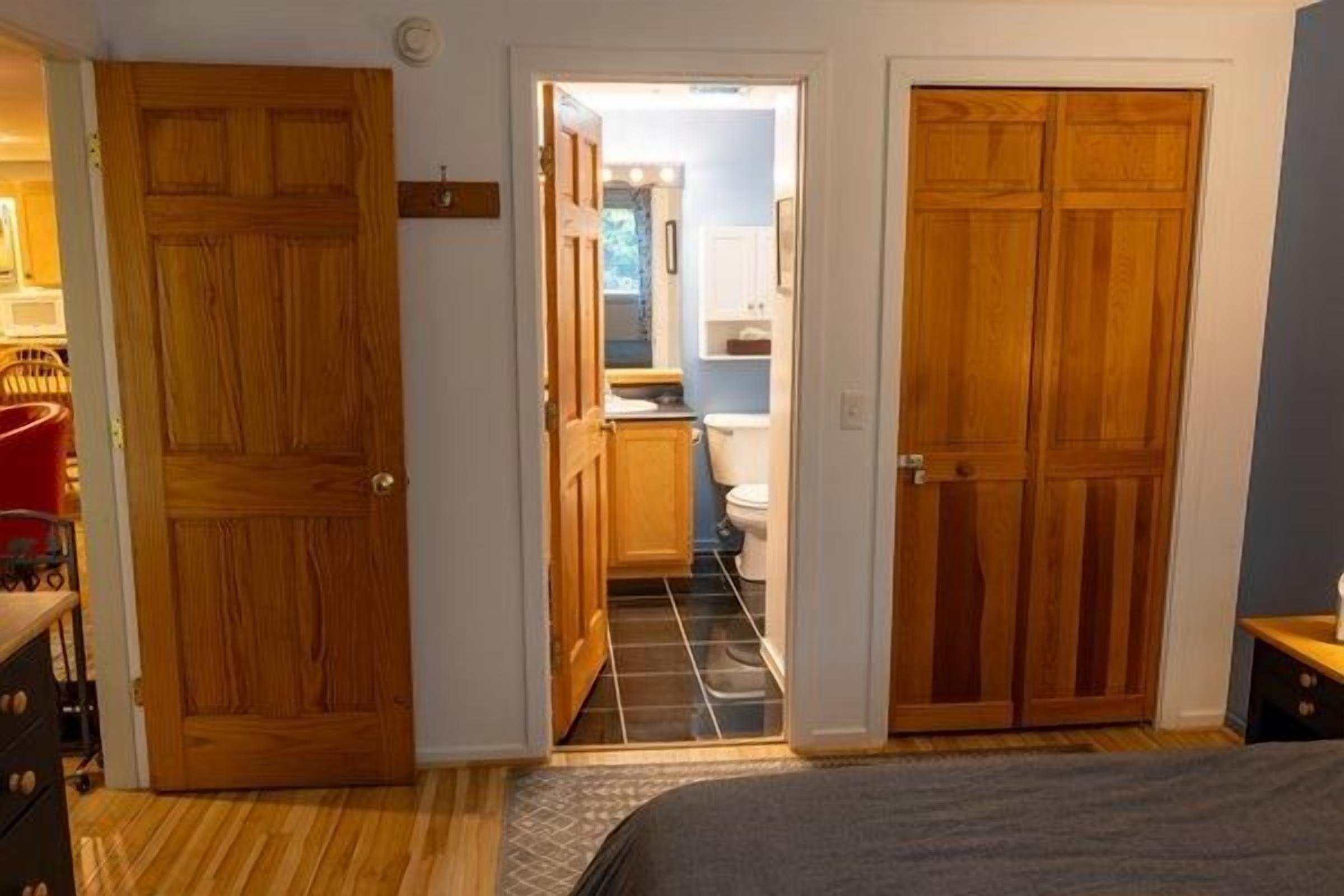 A bedroom with a bed, wooden wardrobe, and a door leading to a bathroom with a toilet and sink.