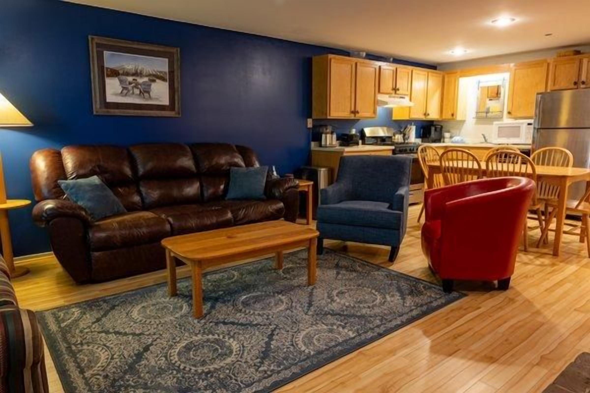 A living room with a brown leather sofa, a blue armchair, a wooden coffee table, and a red chair.