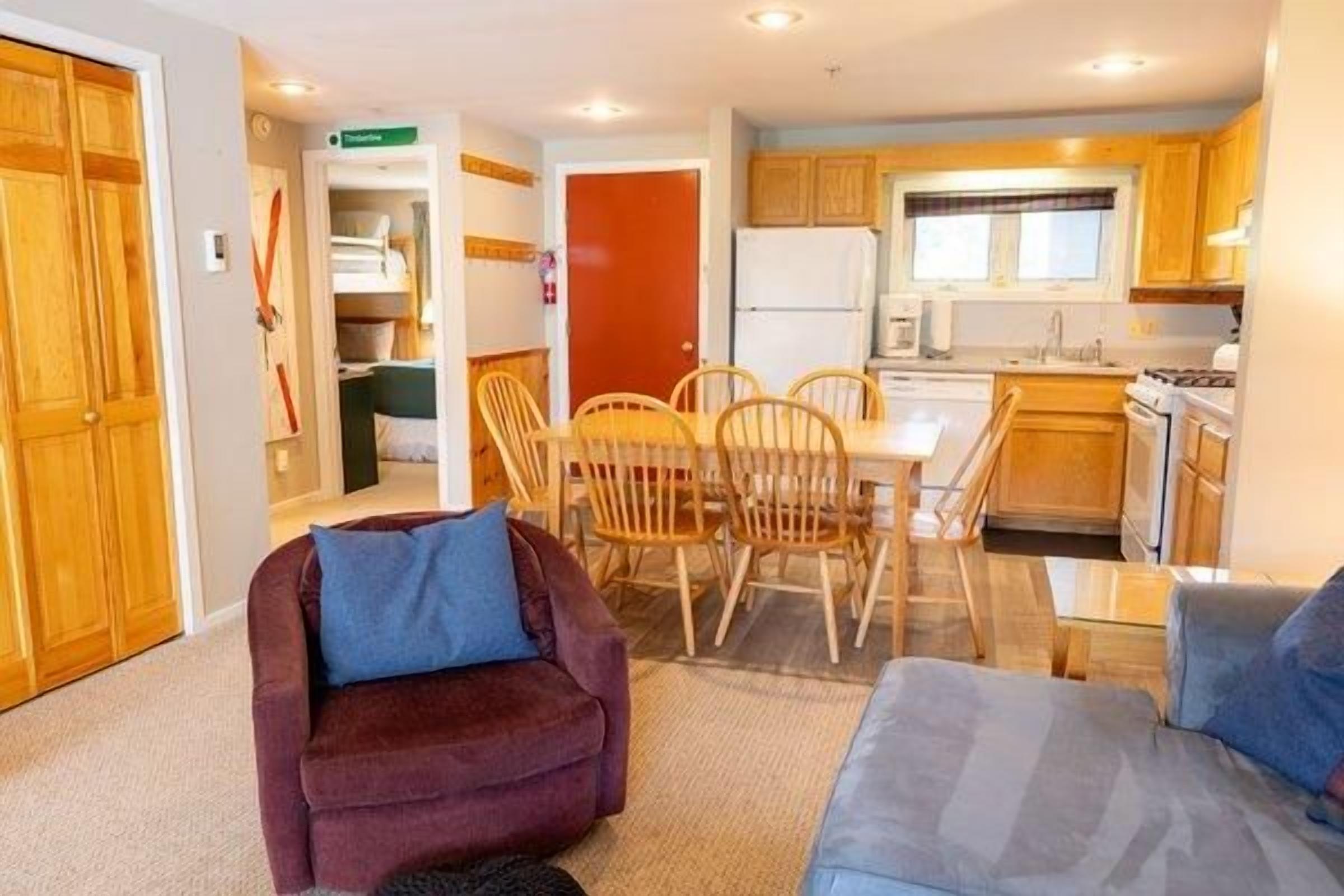 A compact living space with a kitchenette, a dining area with wooden chairs, and a sofa with cushions.