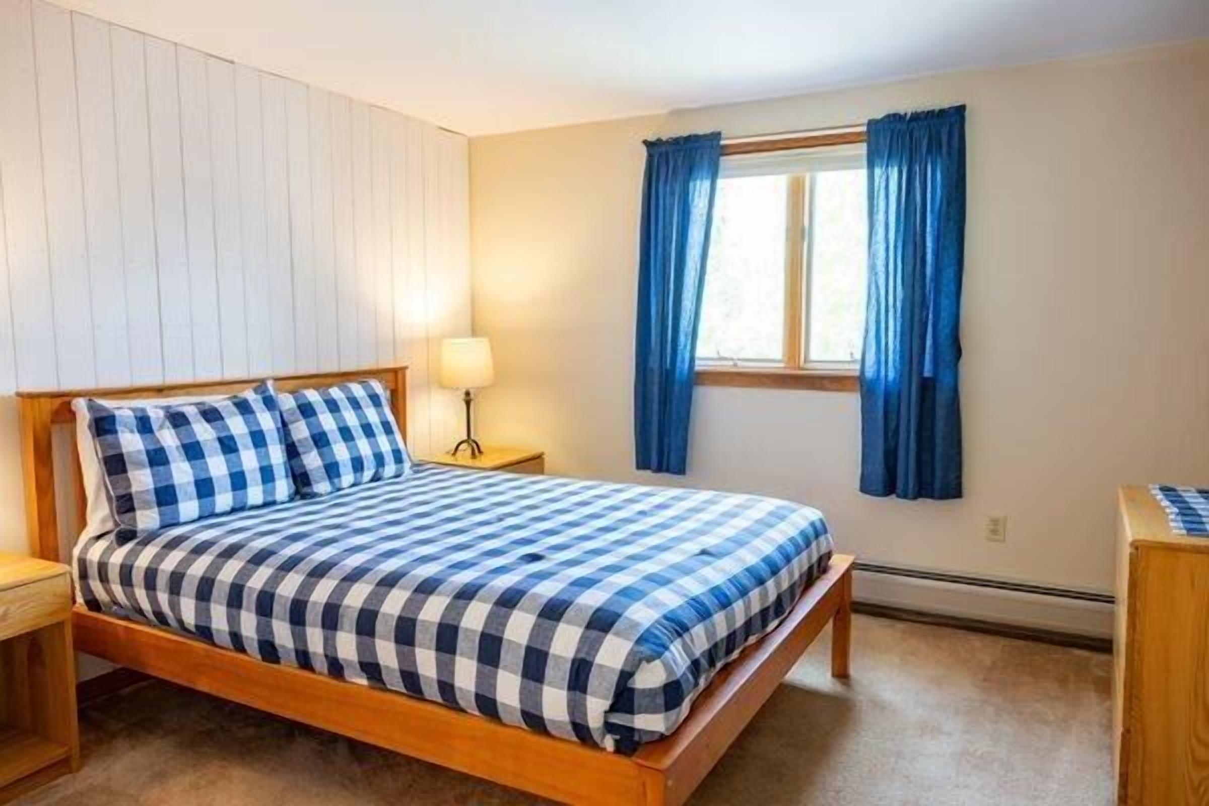 Ein Schlafzimmer mit einem Holzbett, einem Nachttisch, einer Lampe und einem Fenster mit Vorhängen.
