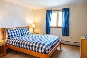 Un dormitorio con cama de madera, una mesita de noche, una lámpara y una ventana con cortinas.