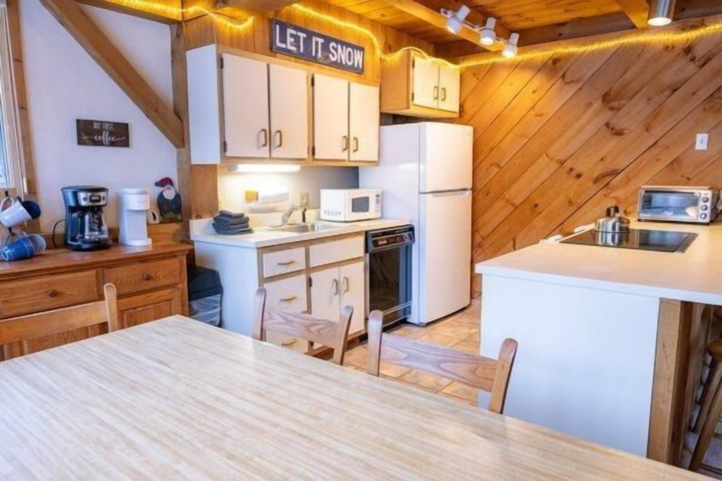 Uma cozinha compacta com armários brancos, micro-ondas, cafeteira e um aviso que diz 'LET IT SNOW'.