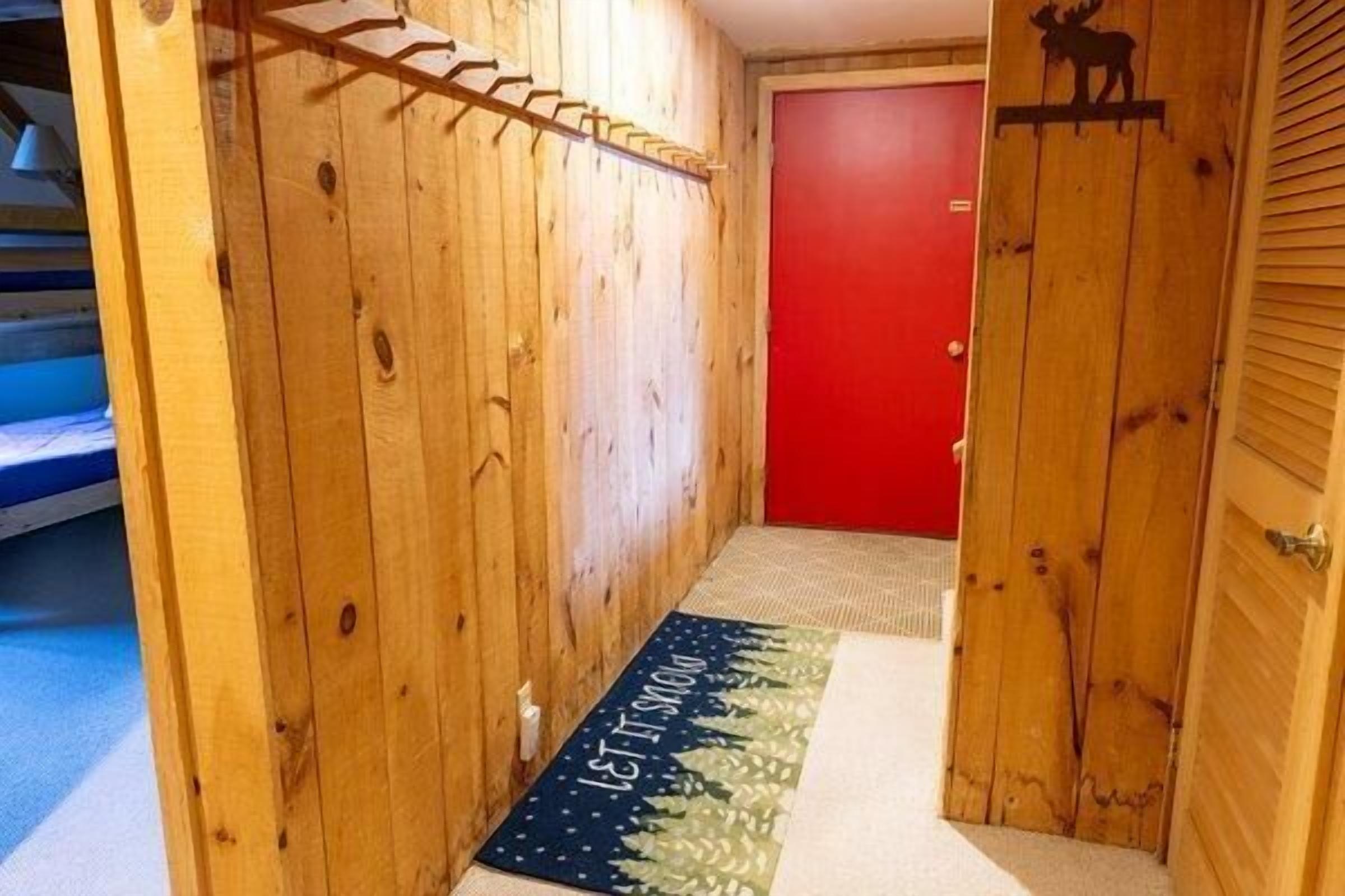 Un pasillo de madera con una puerta roja y un felpudo con la silueta de un alce.