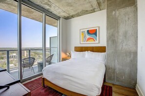 Ein modernes Hotelzimmer mit einem grossen Bett, Blick auf die Stadt durch raumhohe Fenster und minimalistischer Einrichtung.