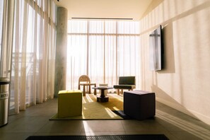 Ein modernes Hotelzimmer mit großem Fenster, Flachbildfernseher, einer Couch, einem Sessel und einem kleinen Tisch.