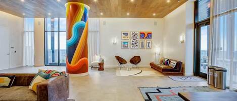 Un soggiorno moderno con un'imponente colonna cilindrica colorata, un divano, due poltrone e opere d'arte alle pareti.