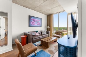 Ein modernes Wohnzimmer mit einer Ledersofa, einem Holztisch, einer blauen TV-Konsole und einem großen Fenster mit Blick ins Freie.