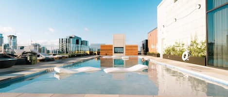 A rooftop pool with a 'NO DIVING 0FT 4IN' sign, lounge chairs, and a city skyline in the background.