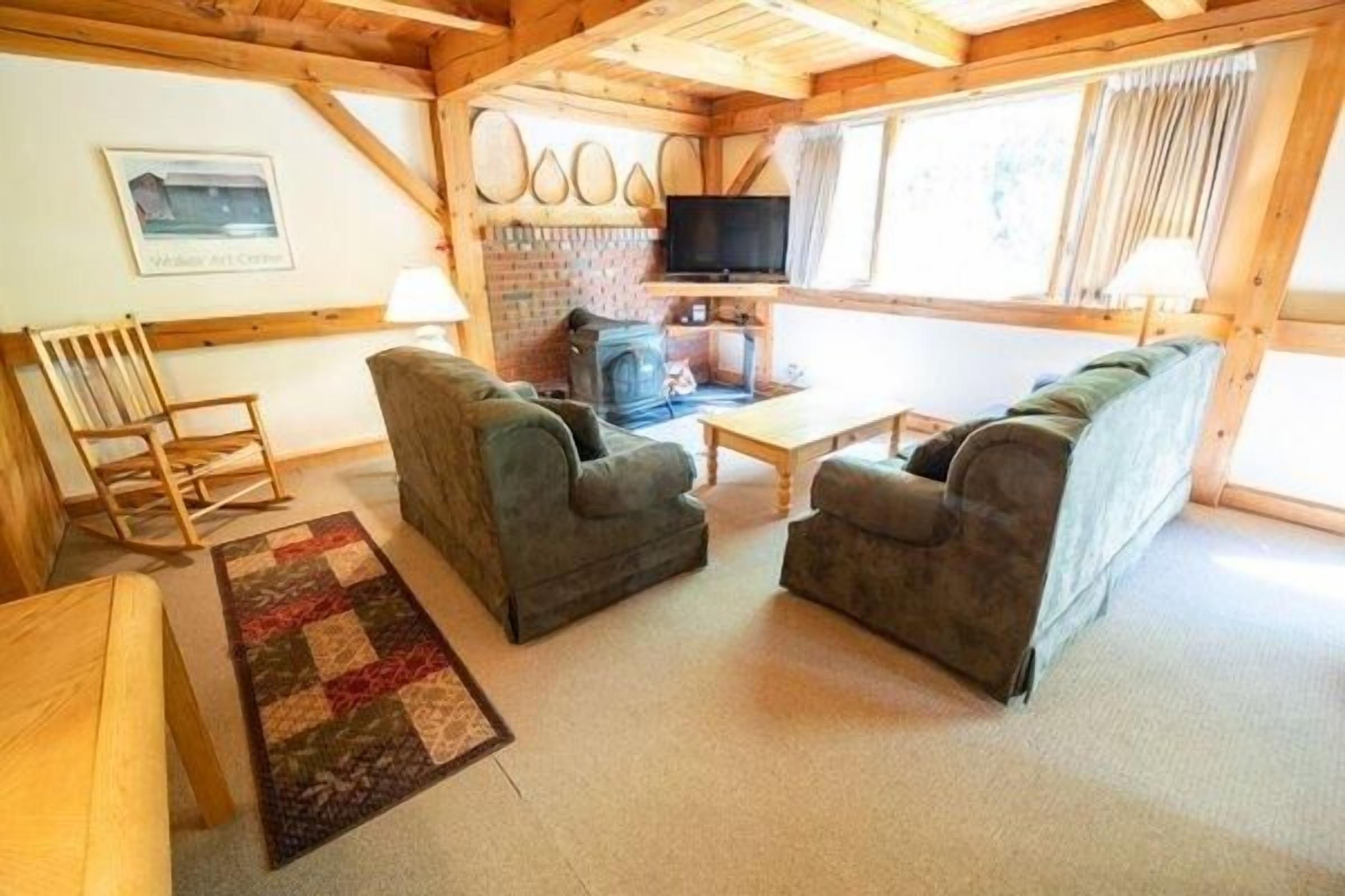 A cozy living room with two sofas, a wooden rocking chair, a television, and a fireplace.