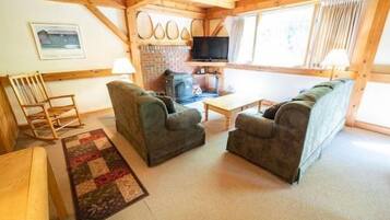 A cozy living room with two sofas, a wooden rocking chair, a television, and a fireplace.