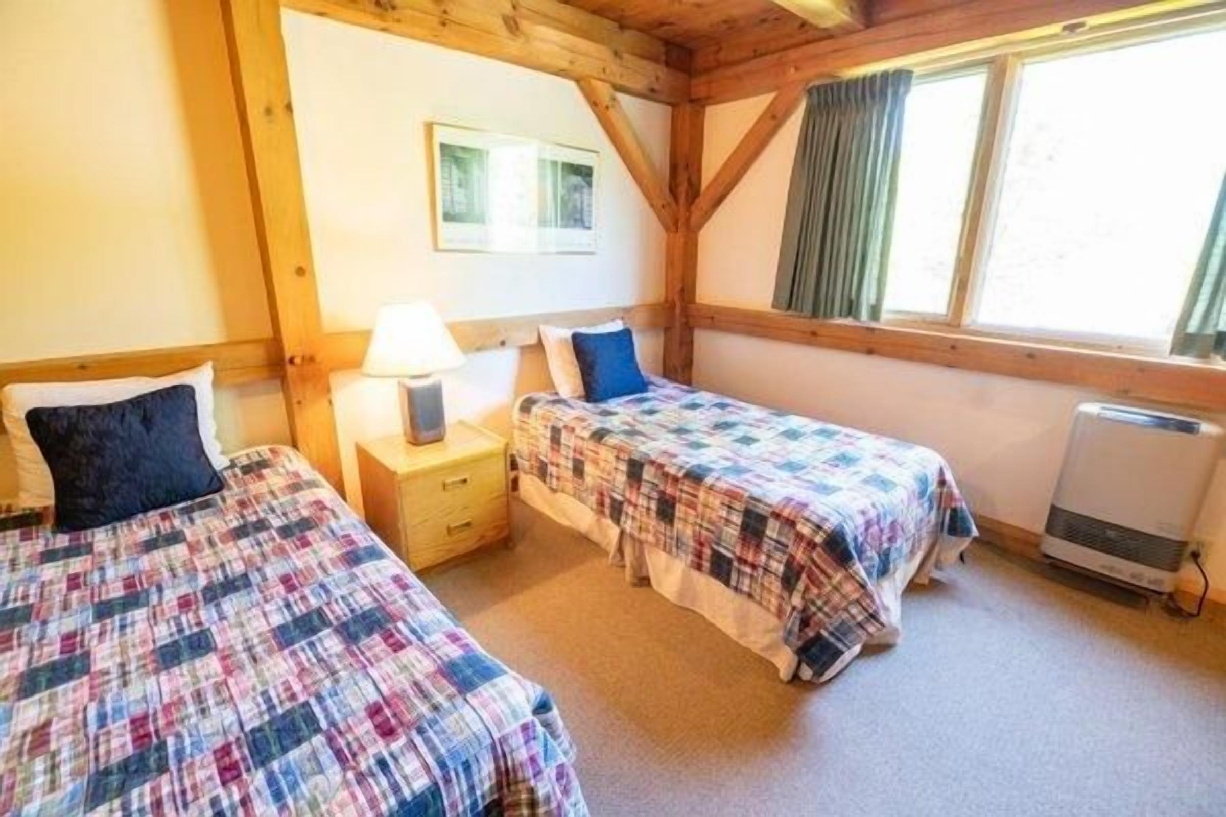 Une chambre avec deux lits, une table de chevet, une lampe et une fenêtre avec des rideaux.