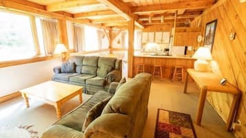 A wooden cabin interior with a sofa, a dining table, and a kitchen area.