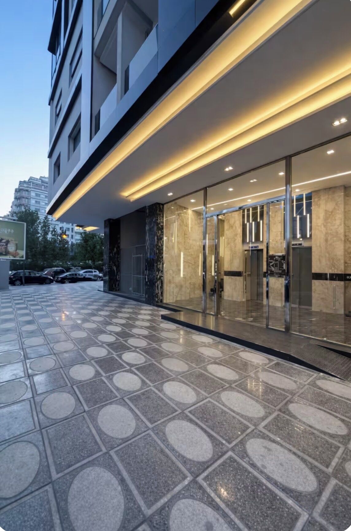 L’entrée moderne d’un hôtel, avec une porte en verre, un sol carrelé et une voiture garée à l’extérieur.