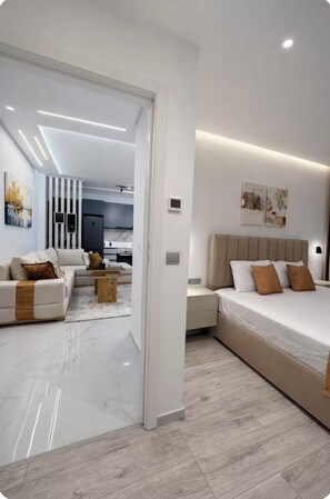 A modern bedroom with a large bed, bedside tables, and a nightstand. There is a sofa and a coffee table in the adjacent living area. - Modern 2BR Apartment with Central AC Near Beach & TGV (Tanger)