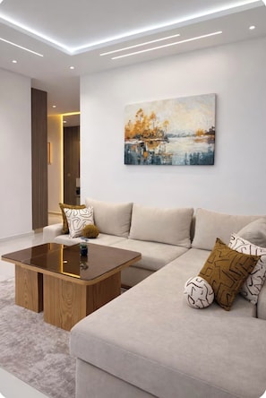 A modern living room with a sectional sofa, a wooden coffee table, and a painting on the wall. - Modern 2BR Apartment with Central AC Near Beach & TGV (Tanger)