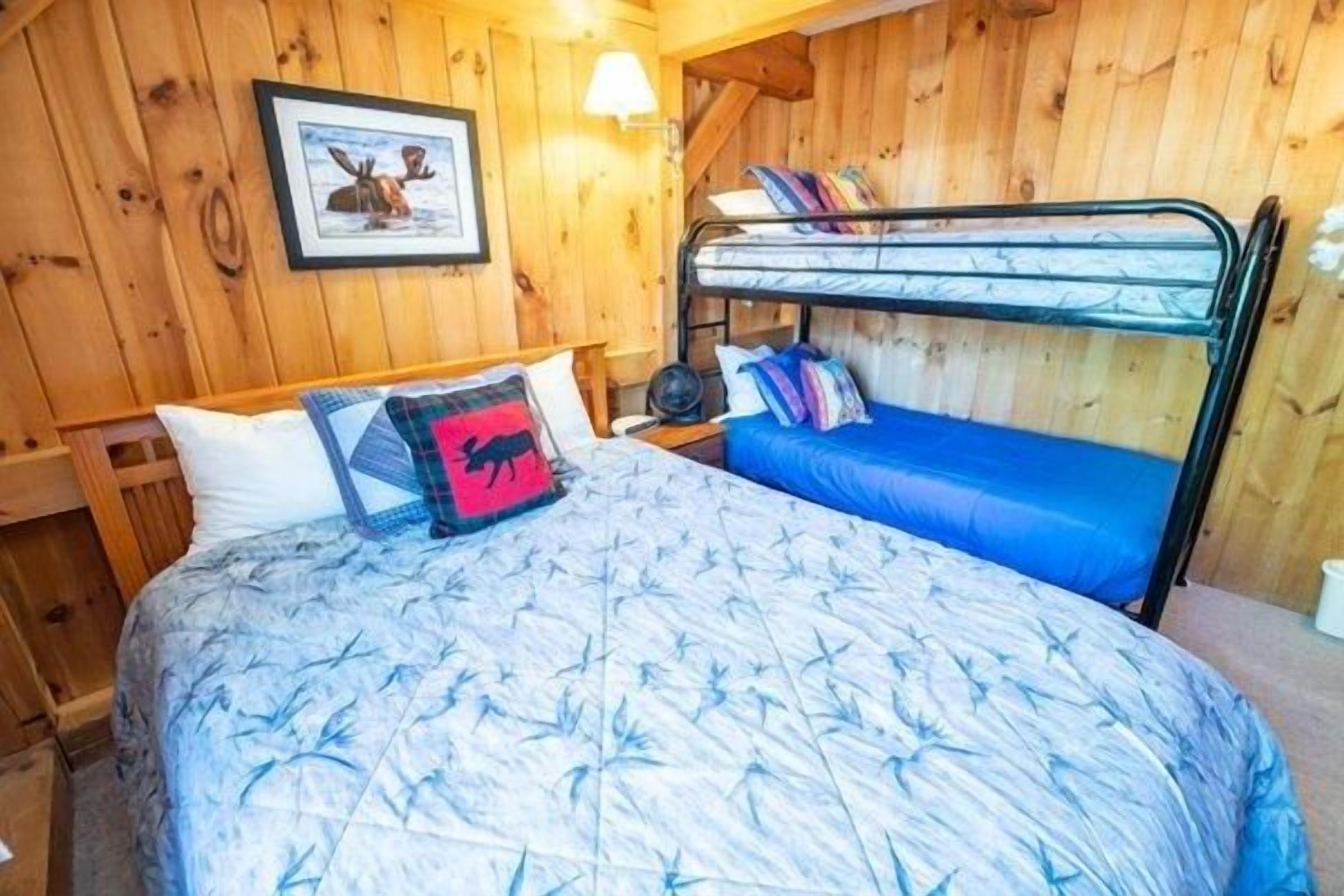Ein Schlafraum mit Etagenbett, einer Holzwand, einem gerahmten Bild und einem Nachttisch.