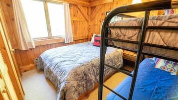 A wooden room with bunk beds, a window with curtains, and a bed with a patterned blanket.