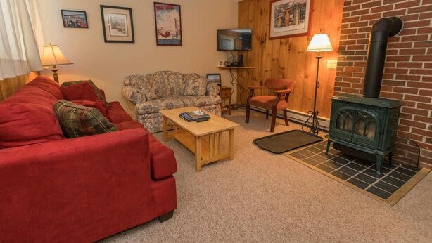 A cozy living room with a red sofa, a patterned armchair, a wooden coffee table, a television, and a brick wall with a fireplace. - Sugarloaf Mountain Birchwood II C827 (Carrabassett Vly)