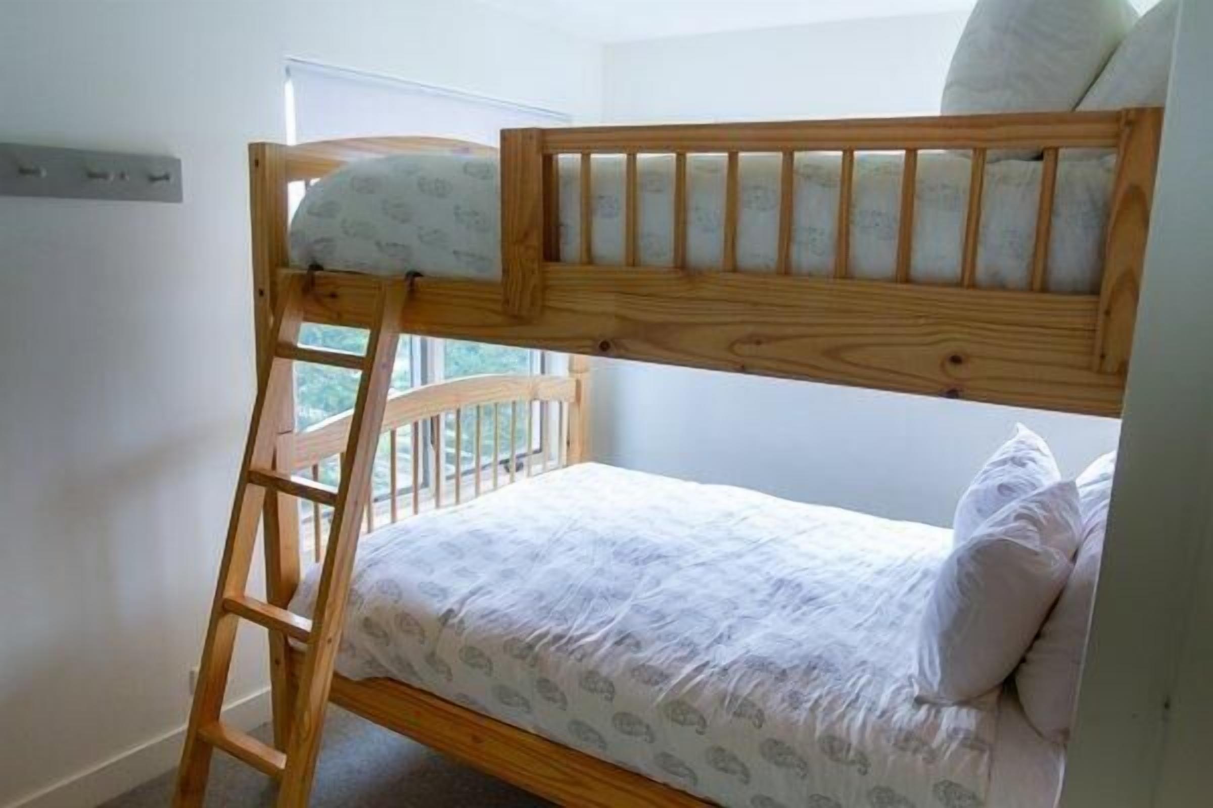 A bunk bed with a wooden ladder, a window with a view, and a white wall.