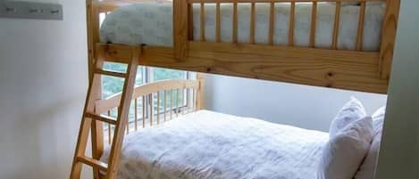 Un lit superposé avec une échelle en bois, une fenêtre donnant sur un beau paysage et un mur blanc.