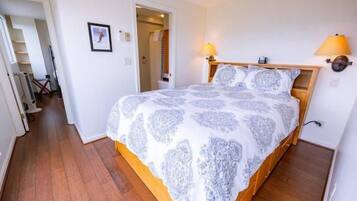 A bedroom with a bed, wooden headboard, bedside lamps, and a door leading to a bathroom.