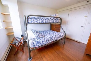A bunk bed with a checkered bedspread, a wooden dresser, and a white door in a room with wooden flooring. - Sugarloaf Mountain Gondola VillageC2209 (Carrabassett Vly)