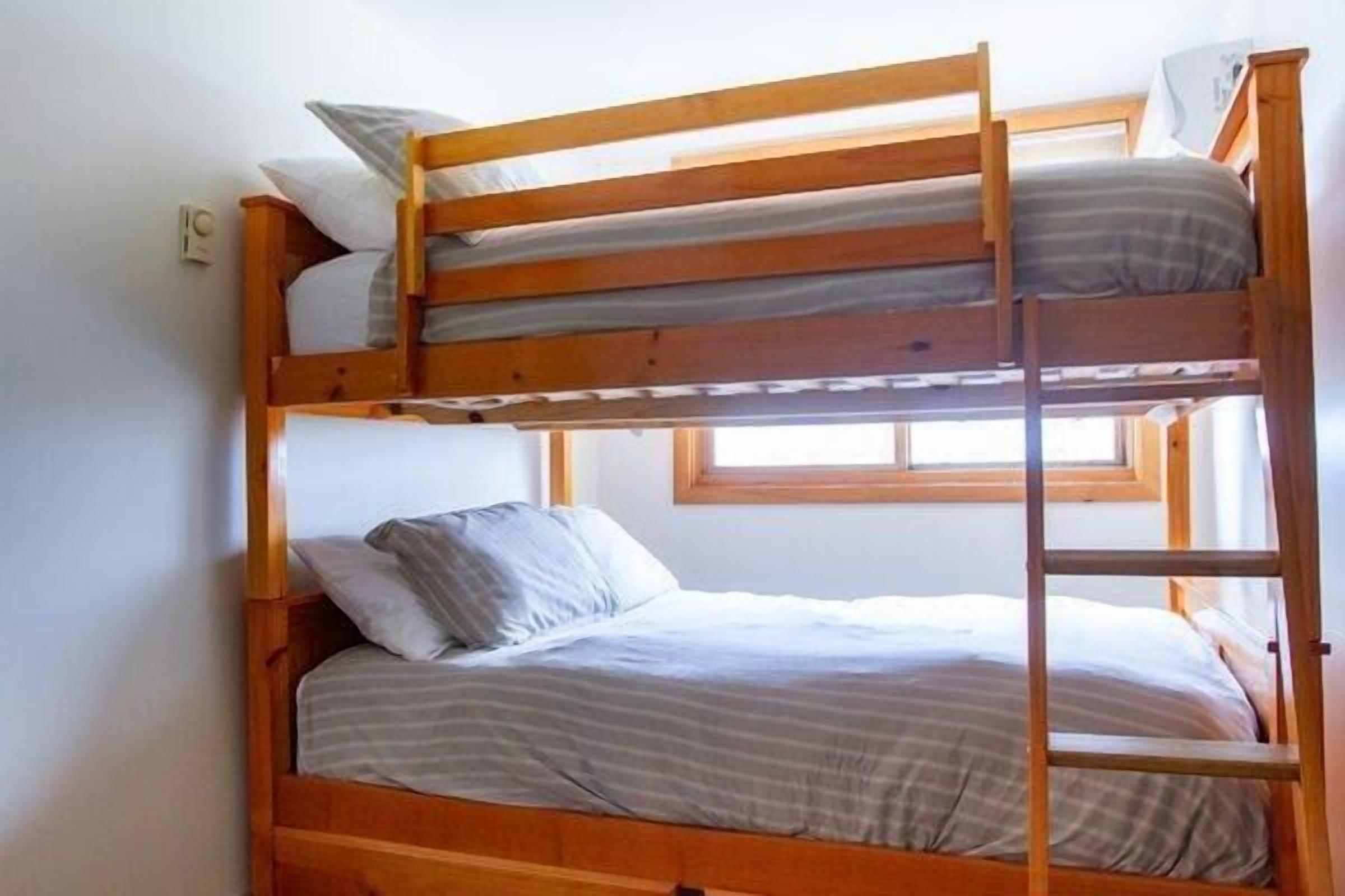 A bunk bed with a ladder, a window, and a wall socket.