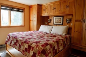 Een slaapkamer met een bed, houten kasten, een raam en een aan de muur hangend schilderij.