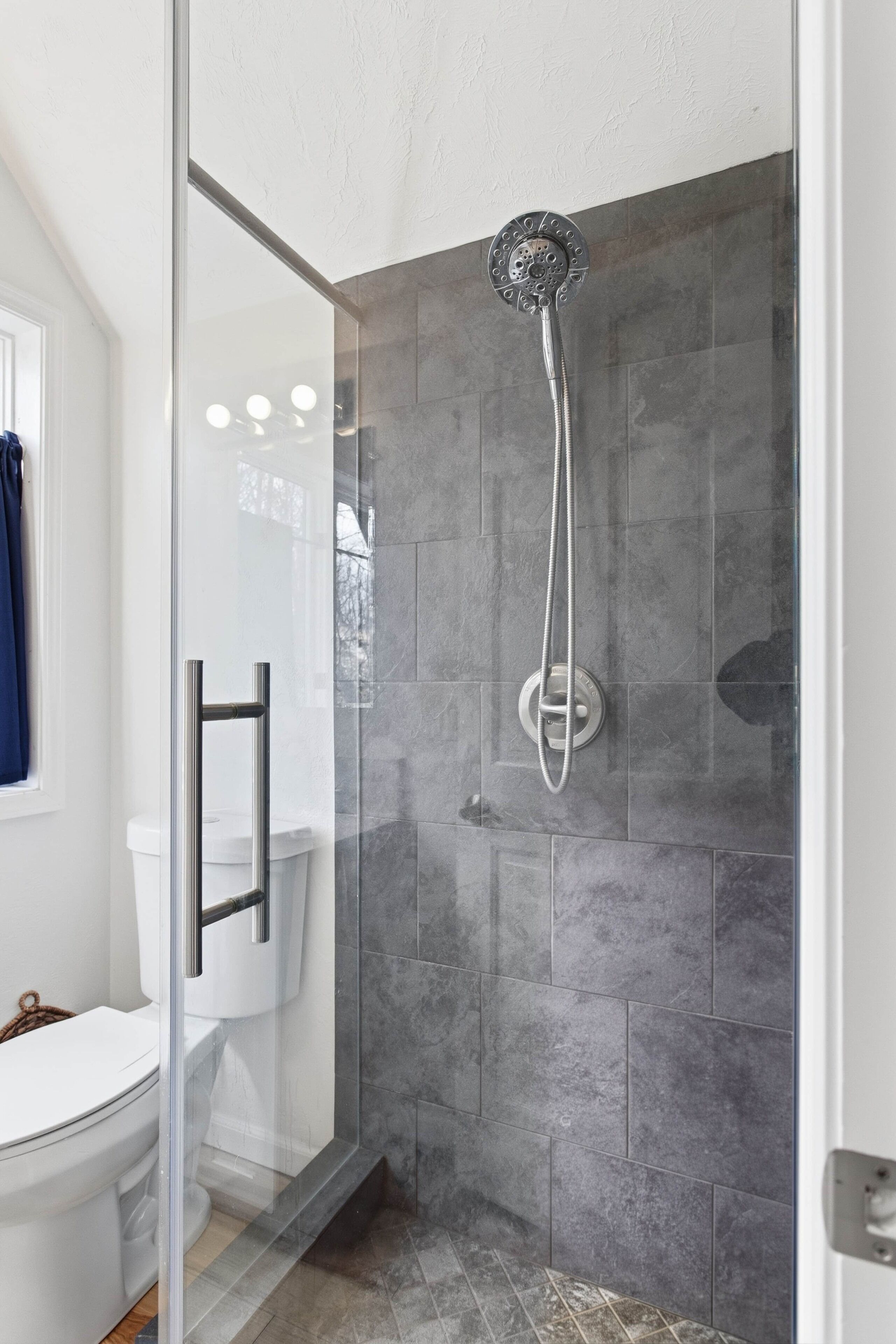 Une salle de bain moderne avec une douche à parois de verre, des murs recouverts de carreaux gris et des toilettes blanches.