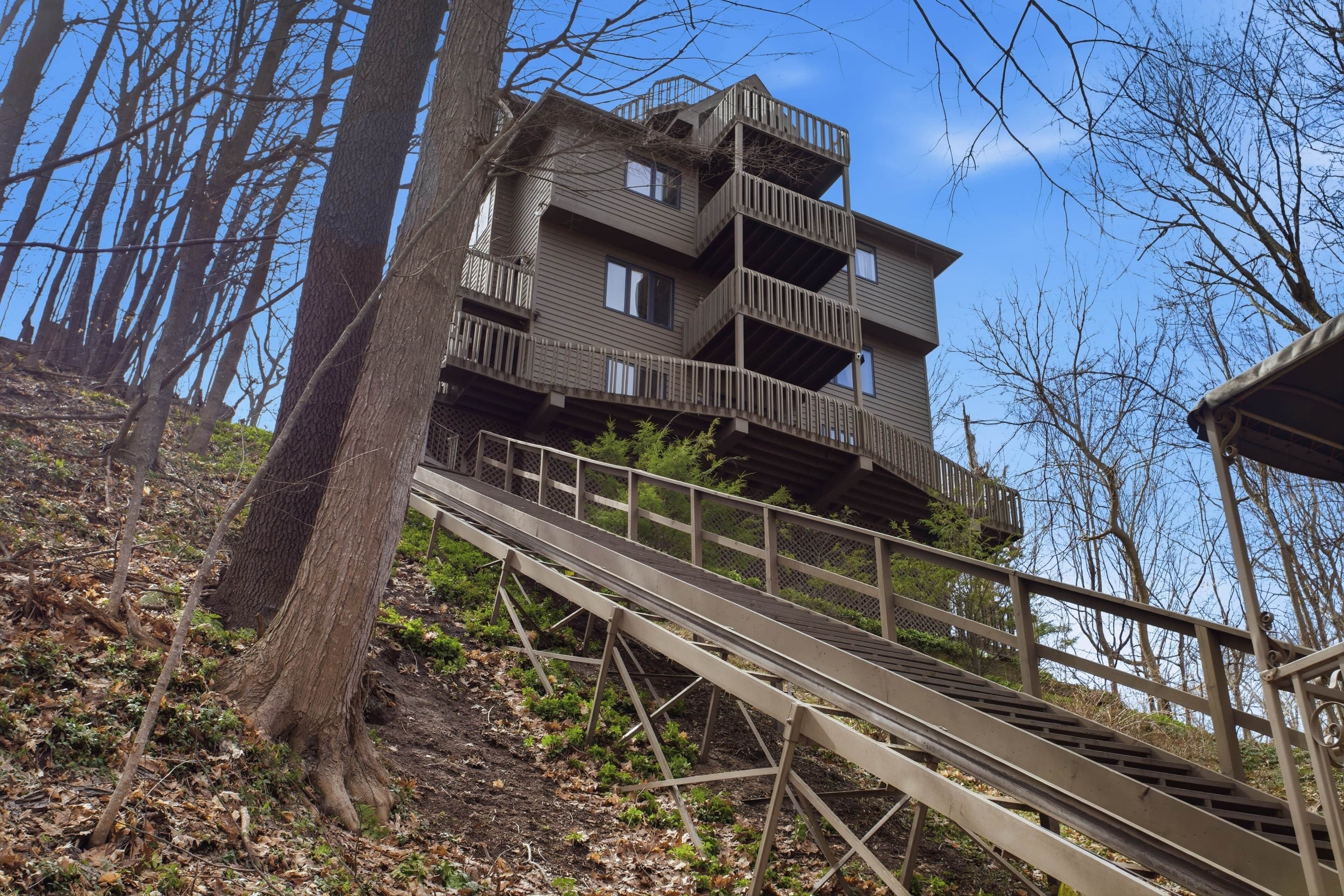 A multi-level wooden building with balconies, surrounded by trees and a wooden walkway leading to it.