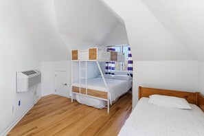 A room with a bunk bed, a single bed, a window with curtains, and a wall-mounted heater. - Wavecrest Cottage-Sleeps 14 Beach (Laketown Township)